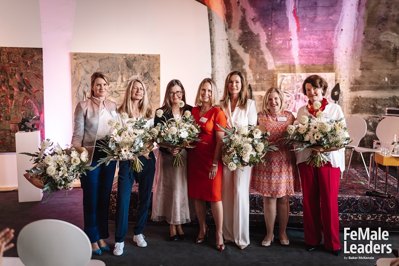 Seven females standing onstage and holding bouquets